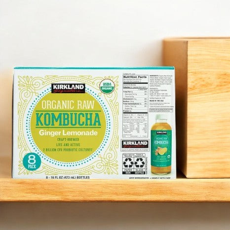 A box of Kirkland Signature Kombucha Organic Ginger Lemonade, packed with probiotics, sits on a wooden shelf, proudly showcasing its packaging and nutrition facts.