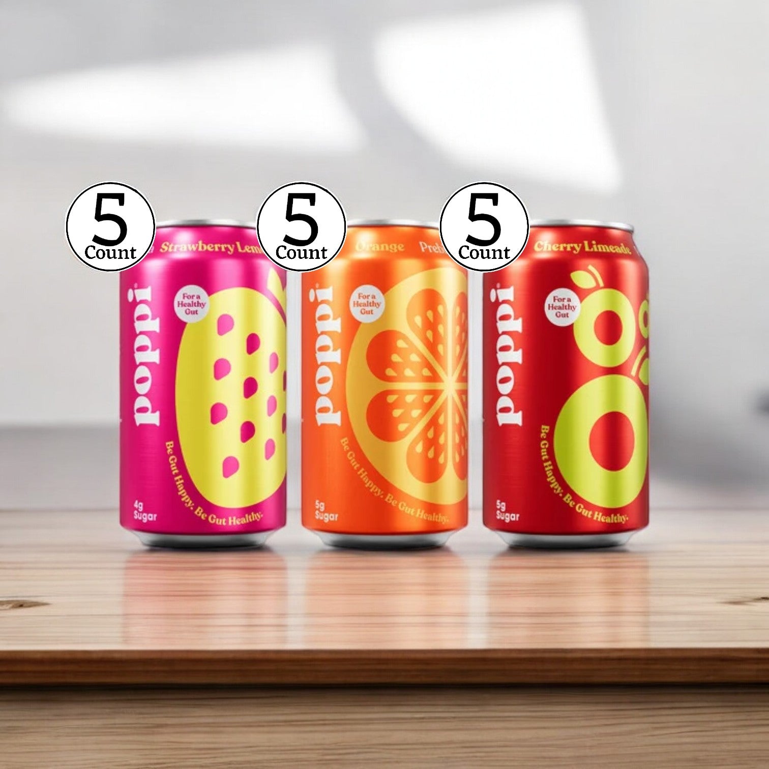 Three low-calorie flavors from the Poppi Prebiotic Soda Variety Pack—Strawberry Lemon, Orange, and Cherry Limeade—are displayed on a wooden surface. Circular "5 Count" labels are above each can, highlighting their support for gut health.