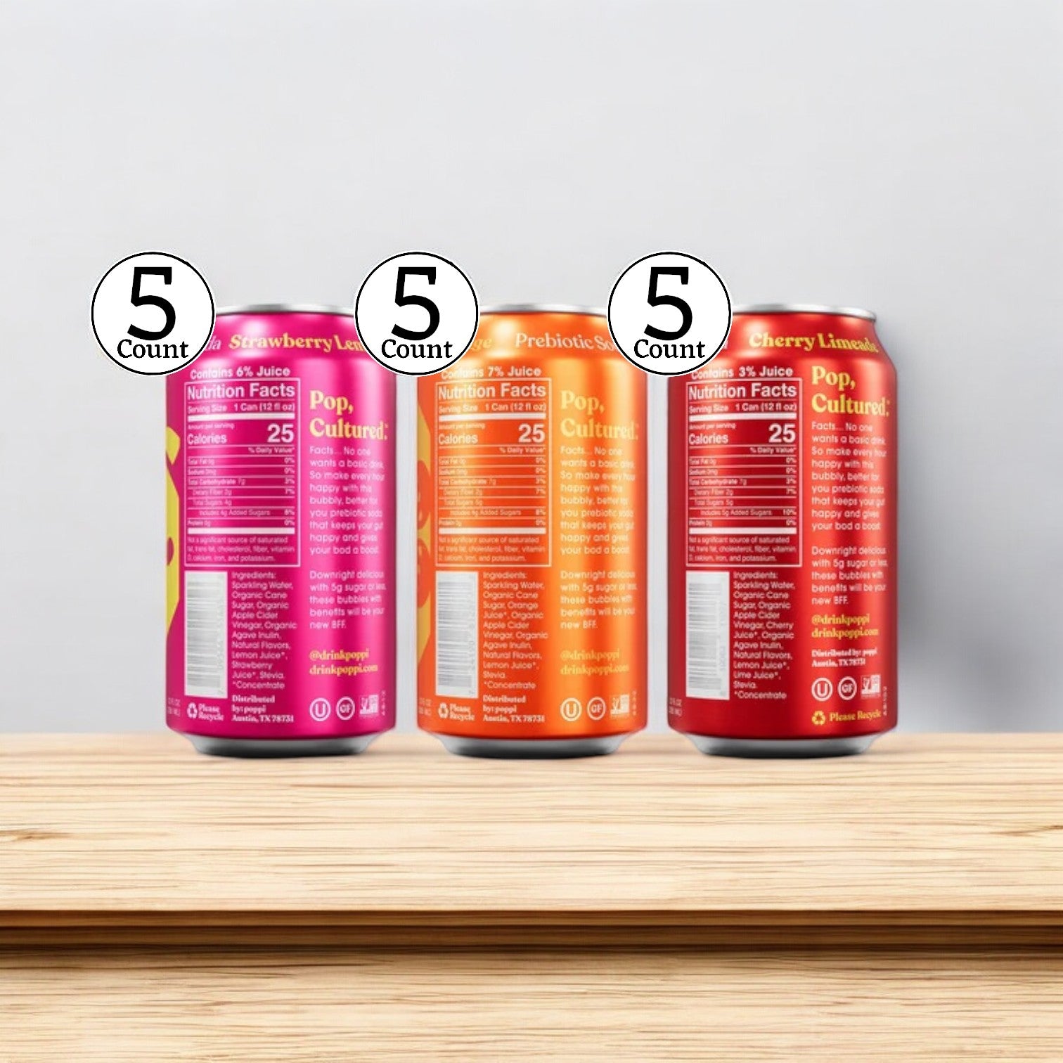 Displayed on a wooden surface is a case of Poppi Prebiotic Soda, Variety Pack, featuring 15 cans in total: 5 Strawberry Lemon, 5 Orange, and 5 Cherry Limeade. These low-calorie drinks promote gut health while tantalizing your taste buds.