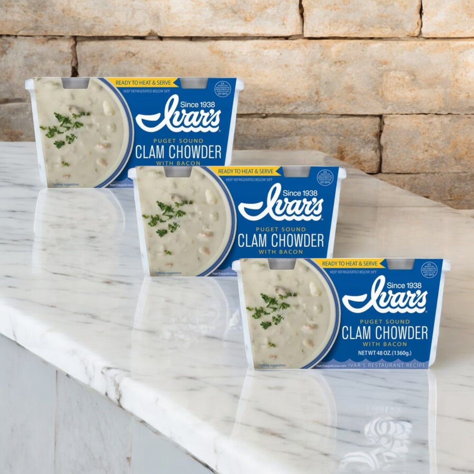 Three boxes of Ivar's Clam Chowder With Bacon are on a marble counter in front of a stone wall.