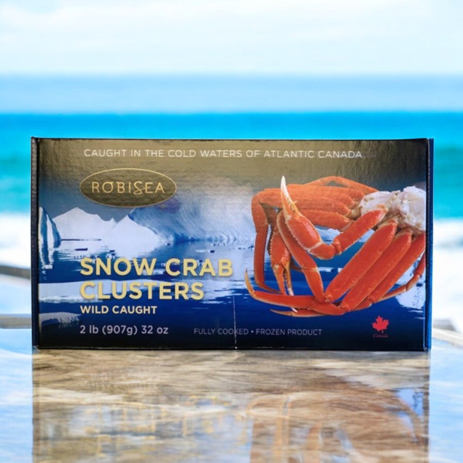 A box of Robisea Wild Caught Snow Crab Clusters, 2 lb. by Easy Lunches is set outdoors against the backdrop of the ocean, offering a taste of the sea. Ideal for your next Surf & Turf Feast, combine these clusters with tender Filet Mignon and succulent Lobster Tails for a remarkable dining experience.