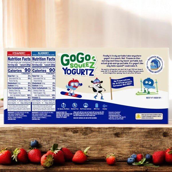 A box of GoGo Squeez Yogurtz Strawberry and Strawberry Banana from Easy Lunches is placed on a wooden table, surrounded by scattered strawberries. The packaging displays the nutrition facts for the Strawberry Banana yogurt flavor and features cartoon characters. Enjoy this delicious, low-fat yogurt treat!