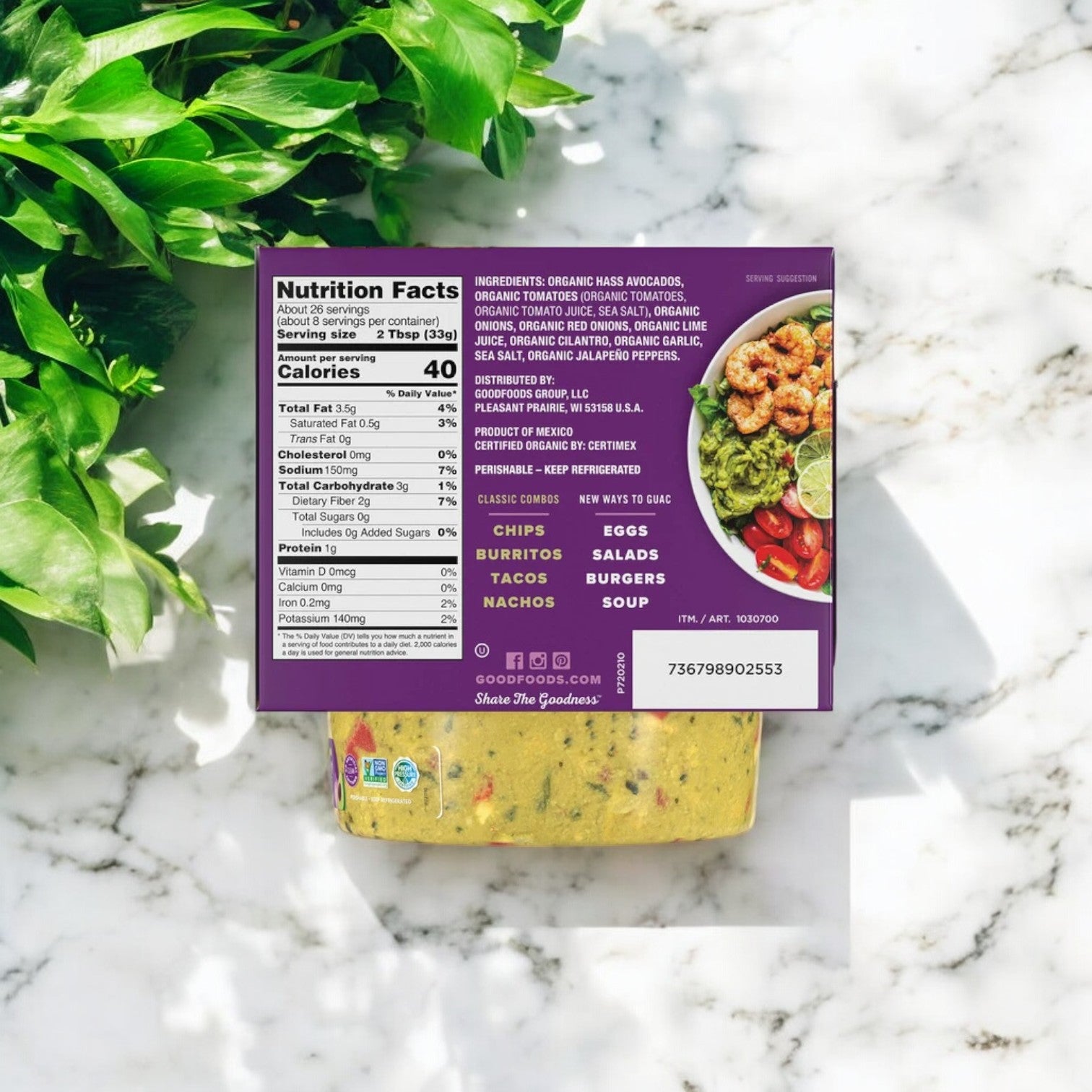 The Good Foods Organic Chunky Guacamole, rich in omega fats from Hass avocados, features a nutrition facts label next to a leafy plant on the marble-textured surface.