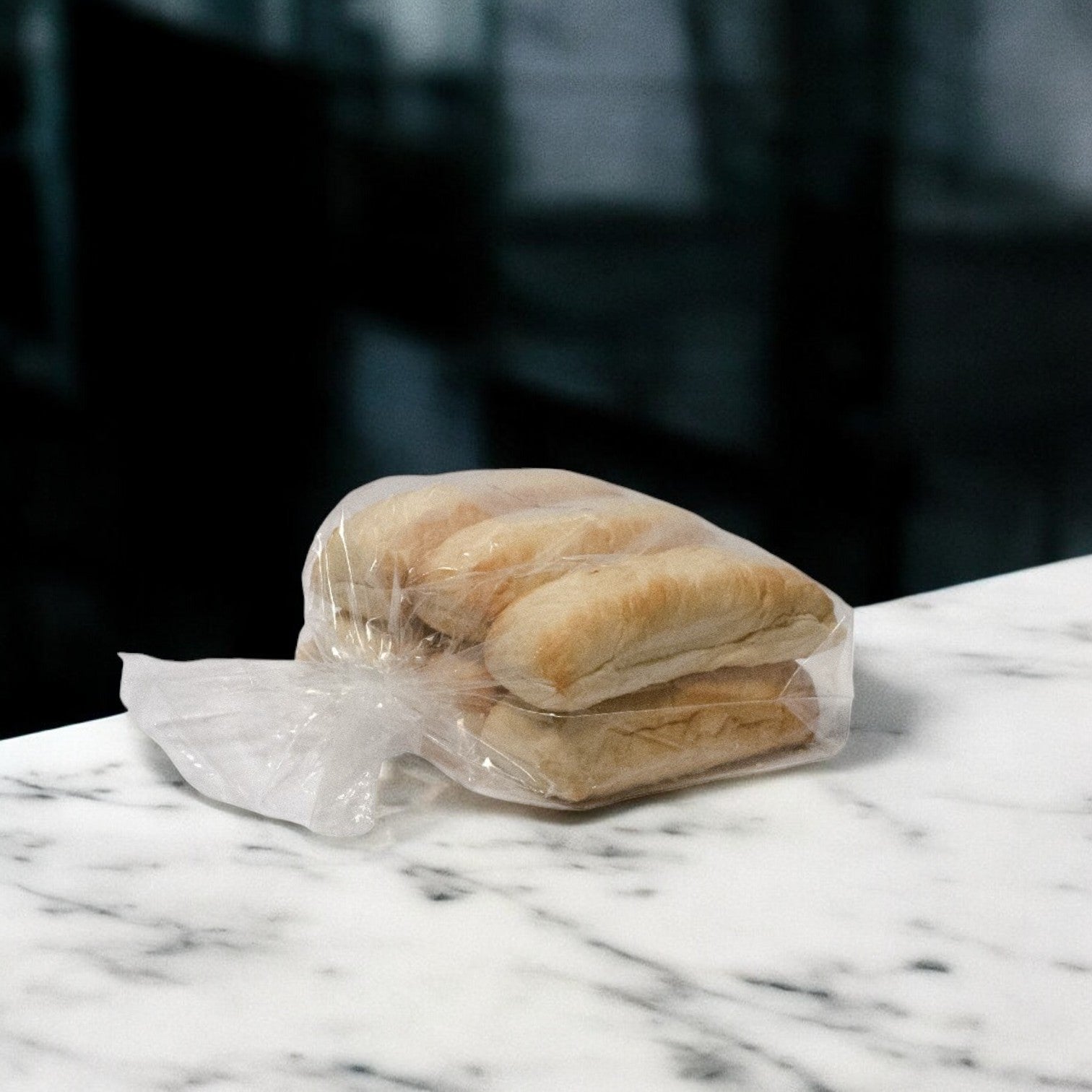 A Buona Beef 8 Pack Kit from Easy Lunches, featuring a plastic bag with four baguettes, sits on a white marble surface, ready to pair with savory Chicago-style Italian beef.