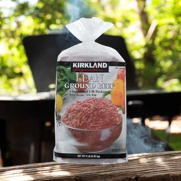 A pack of Kirkland Signature Lean Ground Beef (5 Count - 1 Pack) rests on a wooden surface, ideal for meal prepping, with outdoor furniture and trees softly framing the background.