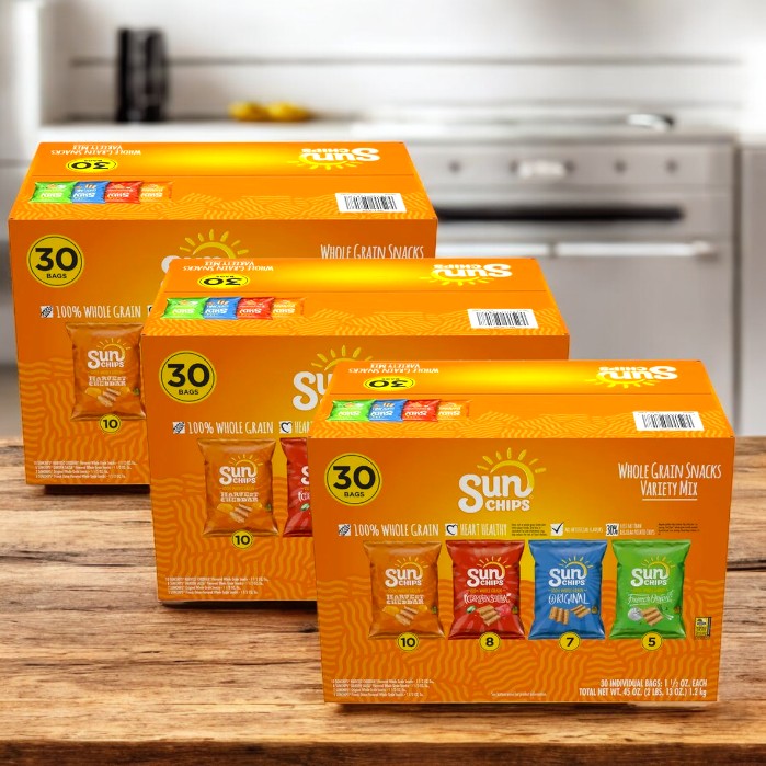 Three boxes of SunChips Variety Pack Whole Grain Chips, totaling 90 bags, are displayed on a wooden kitchen table. Enjoy their wholesome taste without artificial flavors disrupting your snack time bliss.