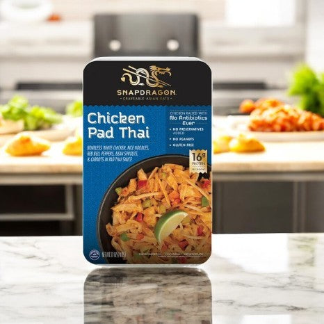 A Snapdragon Chicken Pad Thai, 32 oz-1 Count, rests on the kitchen counter, showcasing noodles, vibrant vegetables, and a lime wedge. It promises an authentic Pad Thai experience from the Snapdragon brand even as a frozen meal.