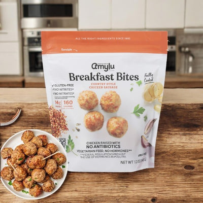On a kitchen counter, a bag labeled Amylu Country Style Chicken Meatballs- 3 Count sits next to a plate of cooked delights, highlighting gluten-free features, protein snack benefits, no nitrites, and just 160 calories per serving.