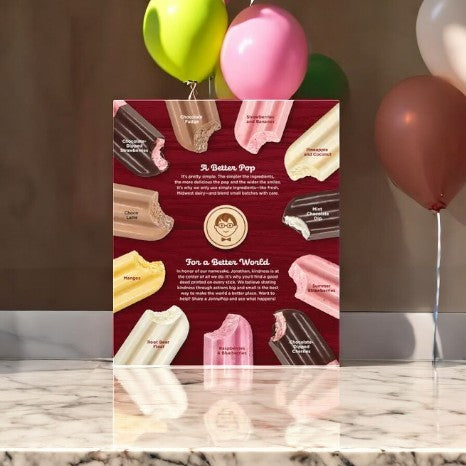 On a marble surface, a square display features Kirkland Signature JonnyPops Chocolate Dipped Cherries With Fresh Cream ice cream bars, adorned with colorful balloons.