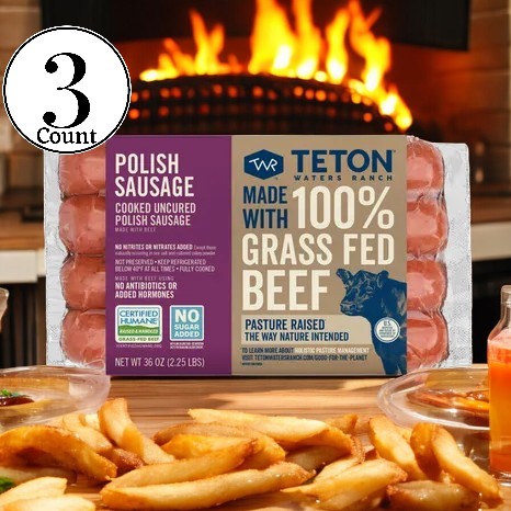 A package of Teton Waters Ranch Polish Sausage- 3 Count, made with 100% grass-fed beef and traditional spices, sits on a kitchen counter. In the foreground are golden fries. The label prominently features the absence of antibiotics or hormones and the use of certified humane practices.