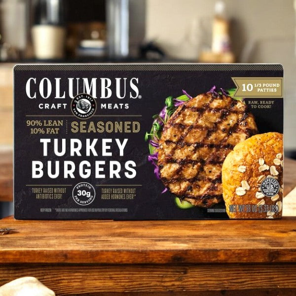 A case of Columbus Seasoned Turkey Burgers (5.33oz, 10-count) by Colombus is shown on a wooden surface, featuring 90% lean protein, 30g protein per serving, and gluten-free labeling for a healthier option.