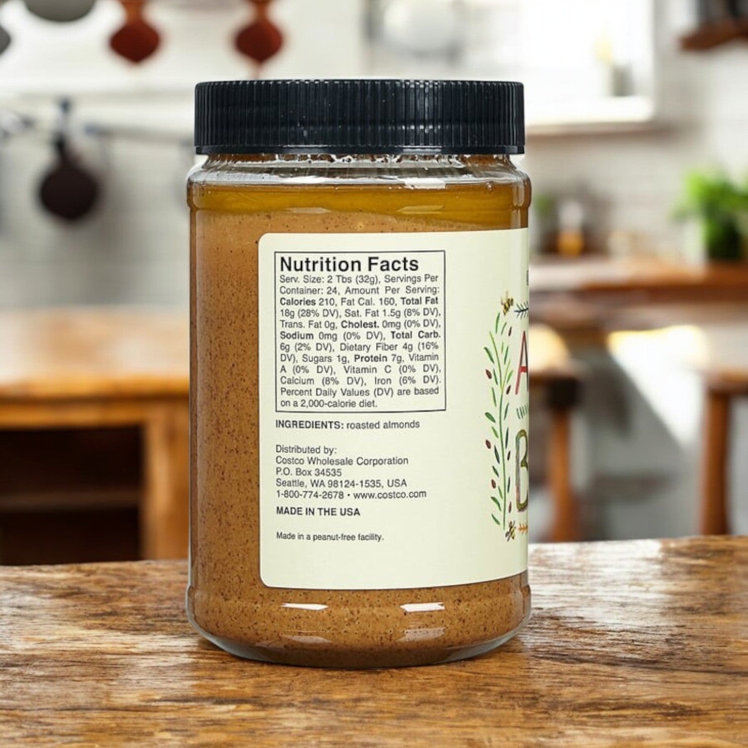 A 27 oz jar from the 3-pack of Kirkland Signature Creamy Almond Butter, gluten-free and rich in protein, sits on a wooden table in a cozy kitchen, with a nutrition facts label on the back.