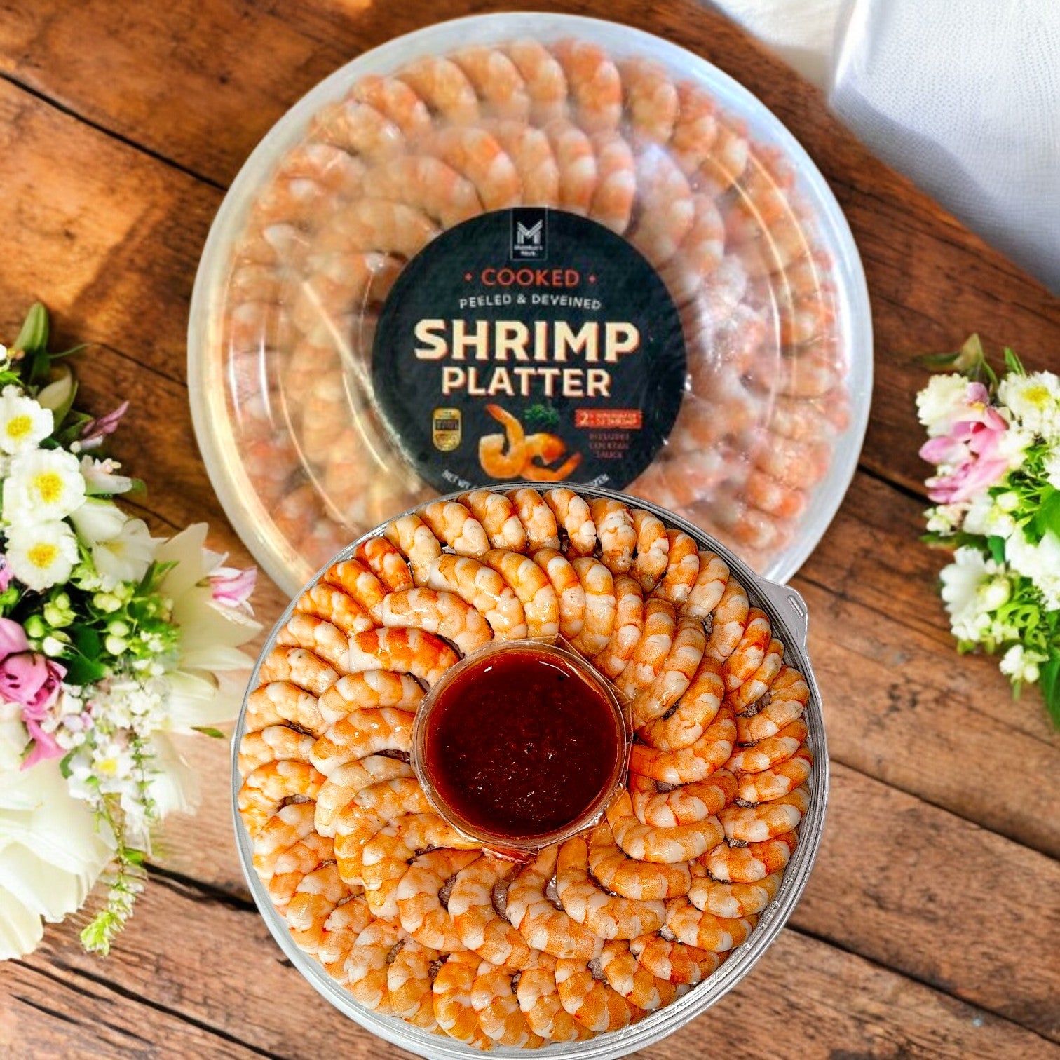 A Member's Mark Shrimp Platter with Cocktail Sauce, Frozen, 2.5 lbs., graces a wooden table amid elegant flower arrangements, inviting you to indulge in its fresh ocean aroma.