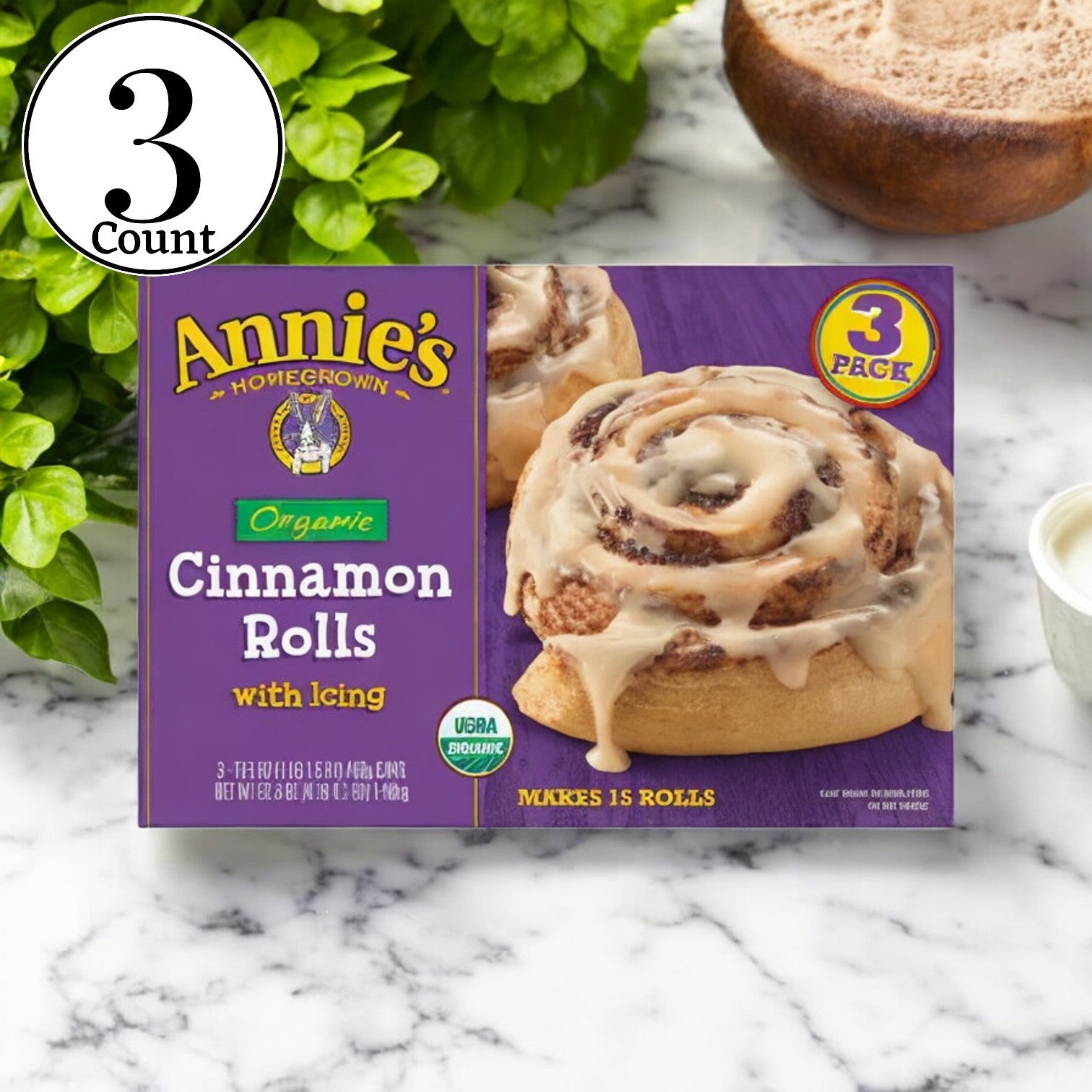 Three boxes of Annie's Organic Cinnamon Rolls, each containing 17.5 oz and three cinnamon rolls, sit on a marble surface, showcasing a tempting treat made with natural ingredients.