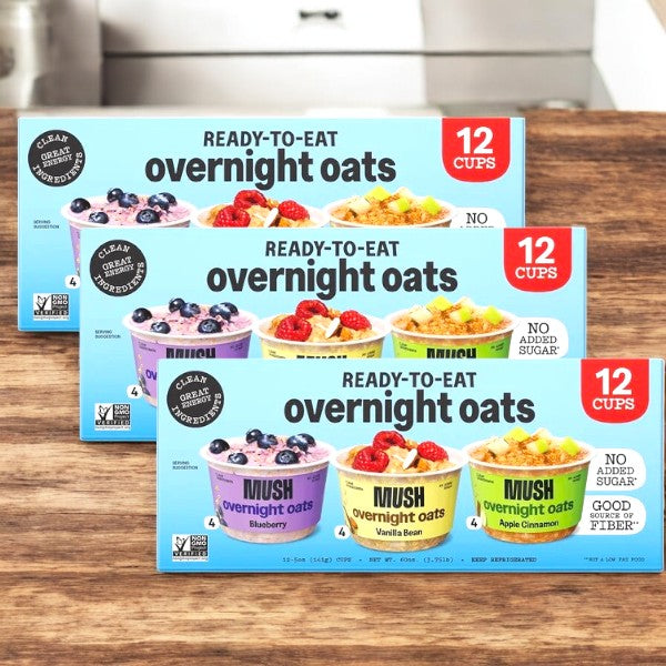 Three cases of Mush Overnight Oats Variety Pack (5 oz, 12-count) are displayed on a wooden surface, featuring blueberry, vanilla bean, and apple cinnamon flavors—perfect for healthy snacks any time.