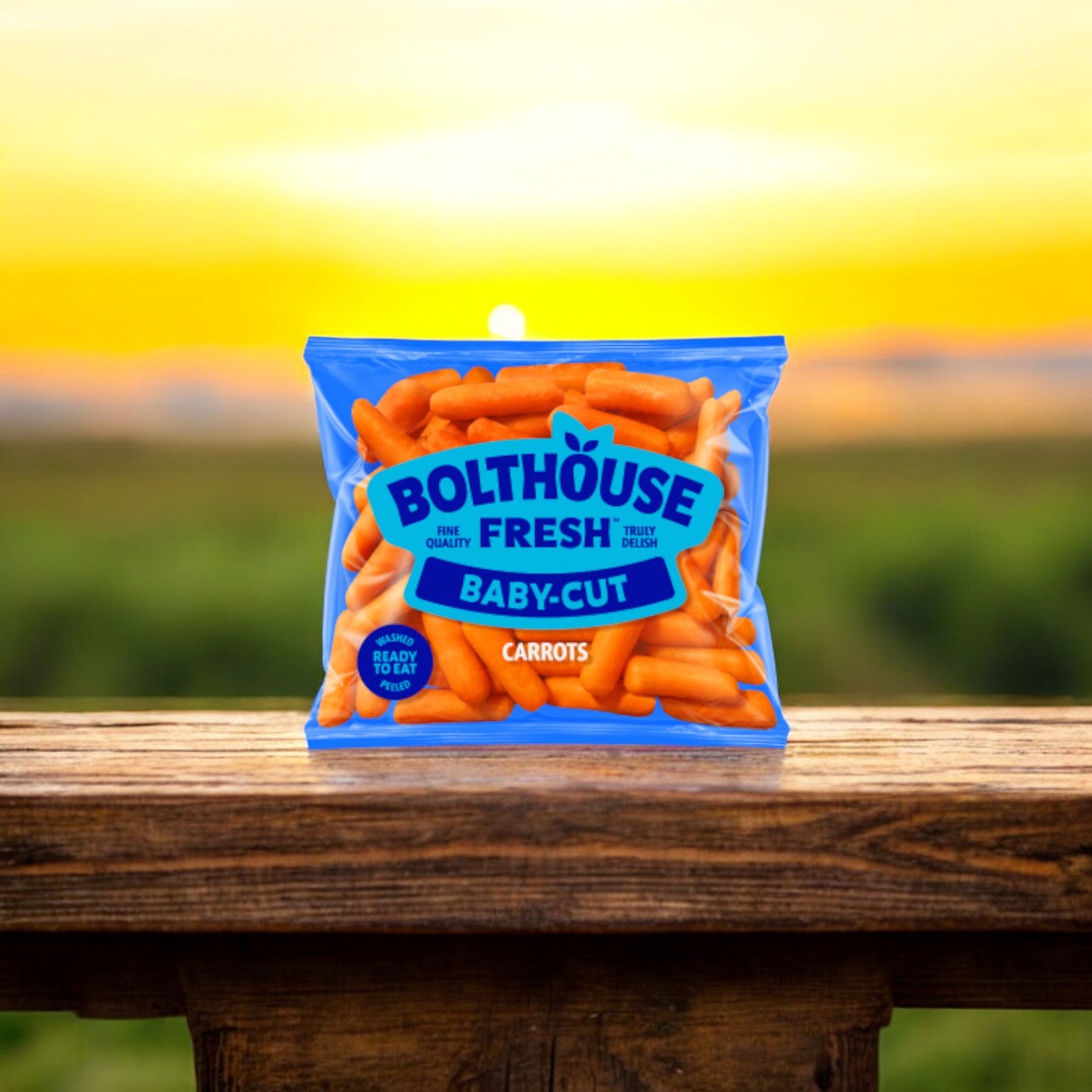 A 1.6 oz pack of Bolthouse Farms Carrots Baby Cut Peeled, nestled on a wooden surface against the backdrop of a picturesque sunset, makes for an excellent and healthy snack choice.