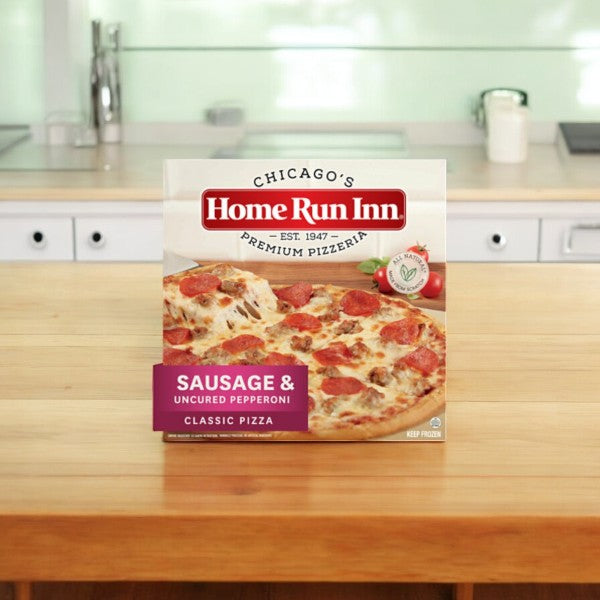 A box of Home Run Inn Family Sausage and Uncured Pepperoni Pizza, weighing 31 oz. from Easy Lunches, featuring premium ingredients and a buttery flaky crust, is displayed on a wooden kitchen counter.