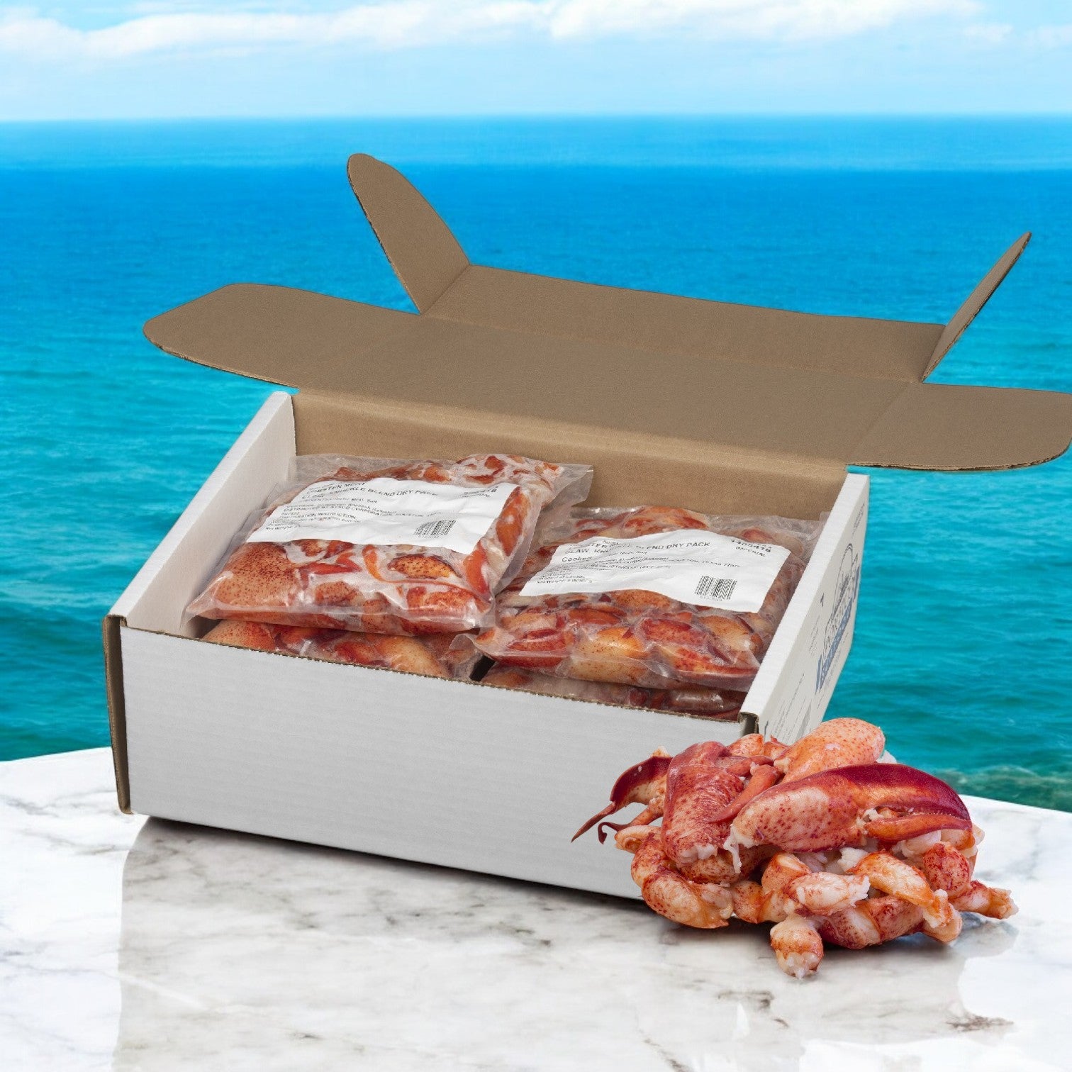 An open cardboard box of dry-packed, sealed Easy Lunches 'Maine Lobster Meat Claw Knuckle' is displayed on a marble surface with the ocean in the background. The set includes 6 packs, each 2 pounds, totaling 12 pounds.