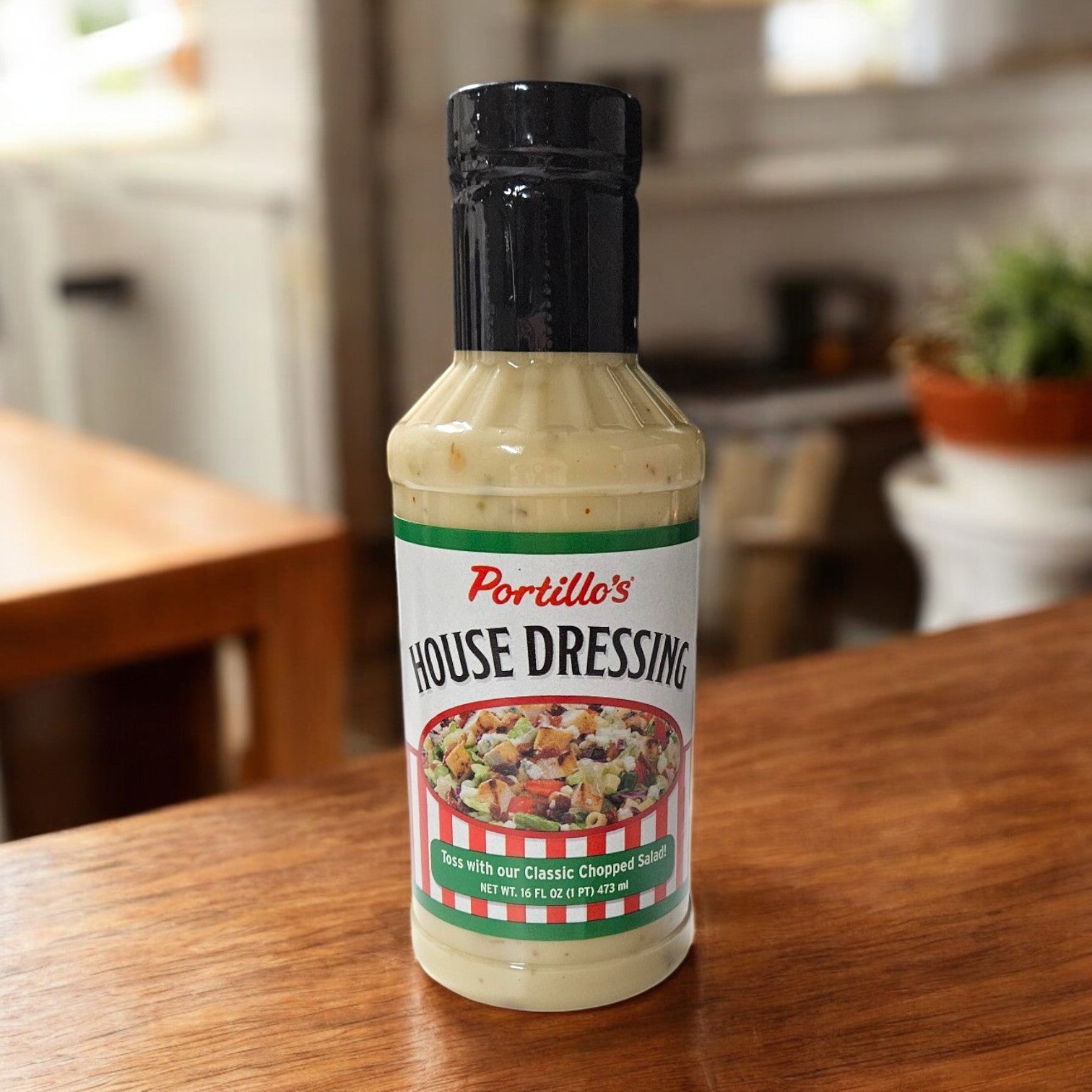 A 16 oz. Portillo's Bottle of House Dressing rests on a wooden table, embodying Chicago-style cuisine, with a blurred indoor backdrop.