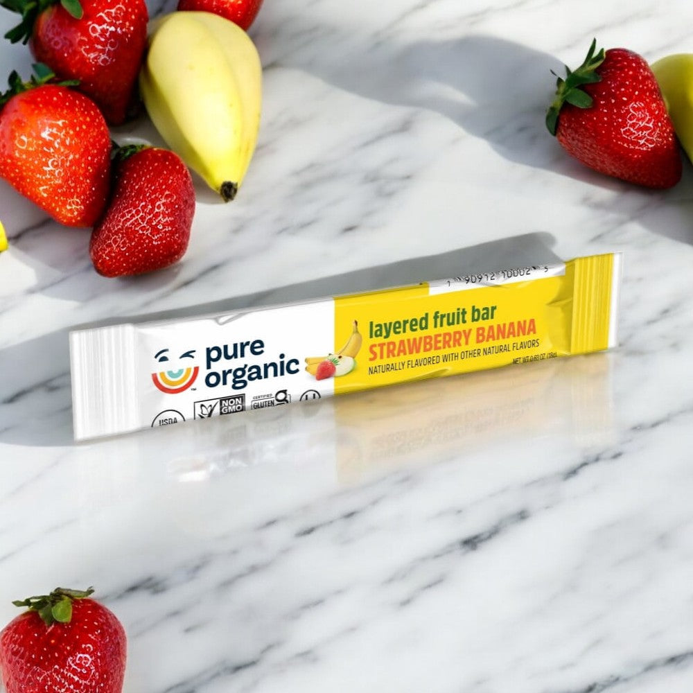 A Pure Organic Strawberry Banana Layered Fruit Bar on a marble surface surrounded by fresh strawberries and a banana. This healthy on-the-go snack from Pure Organic is perfect for those seeking vegan and gluten-free snacks.