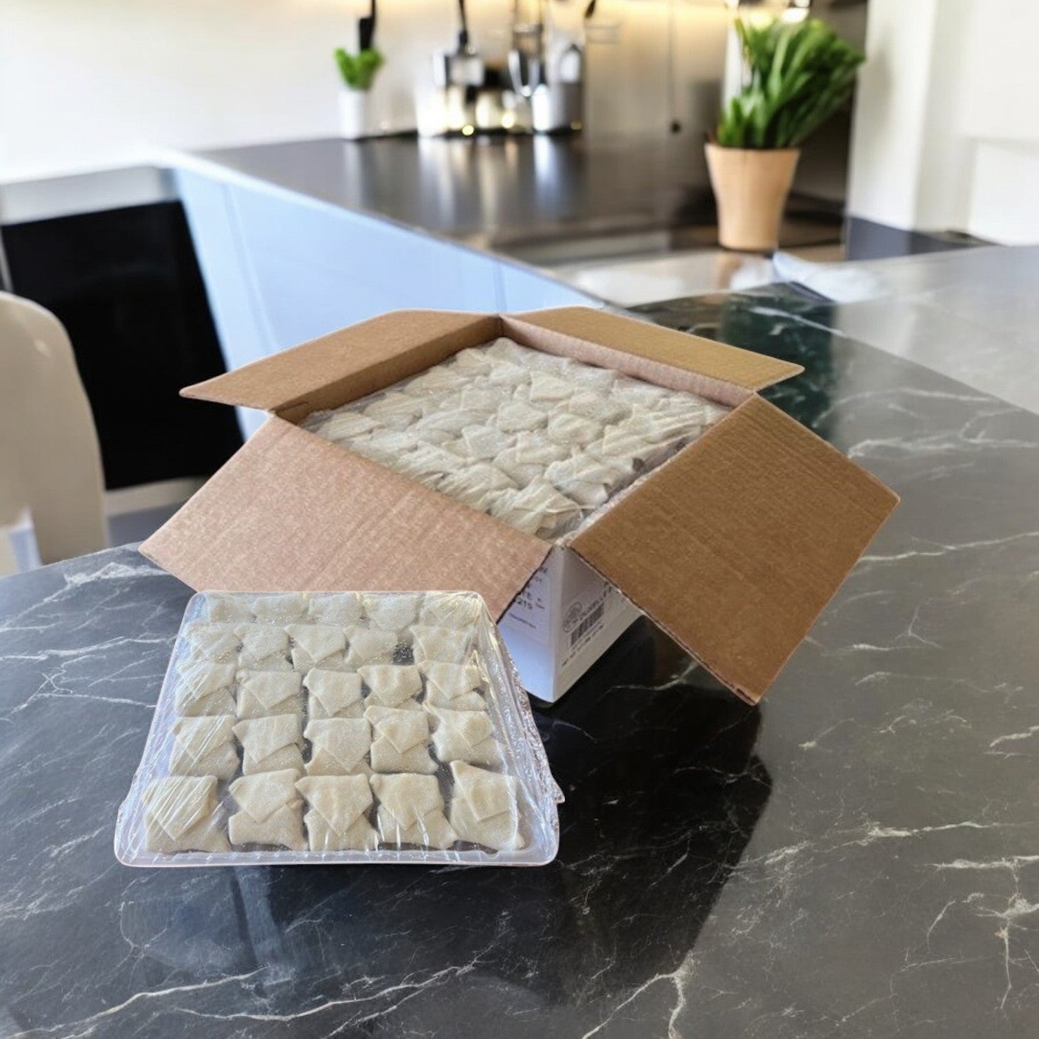 A Sysco Deluxe Beef Wellington appetizer box, open to display individually wrapped squares on a marble countertop, sits amid kitchen appliances, set for creating or serving puff pastry delights.