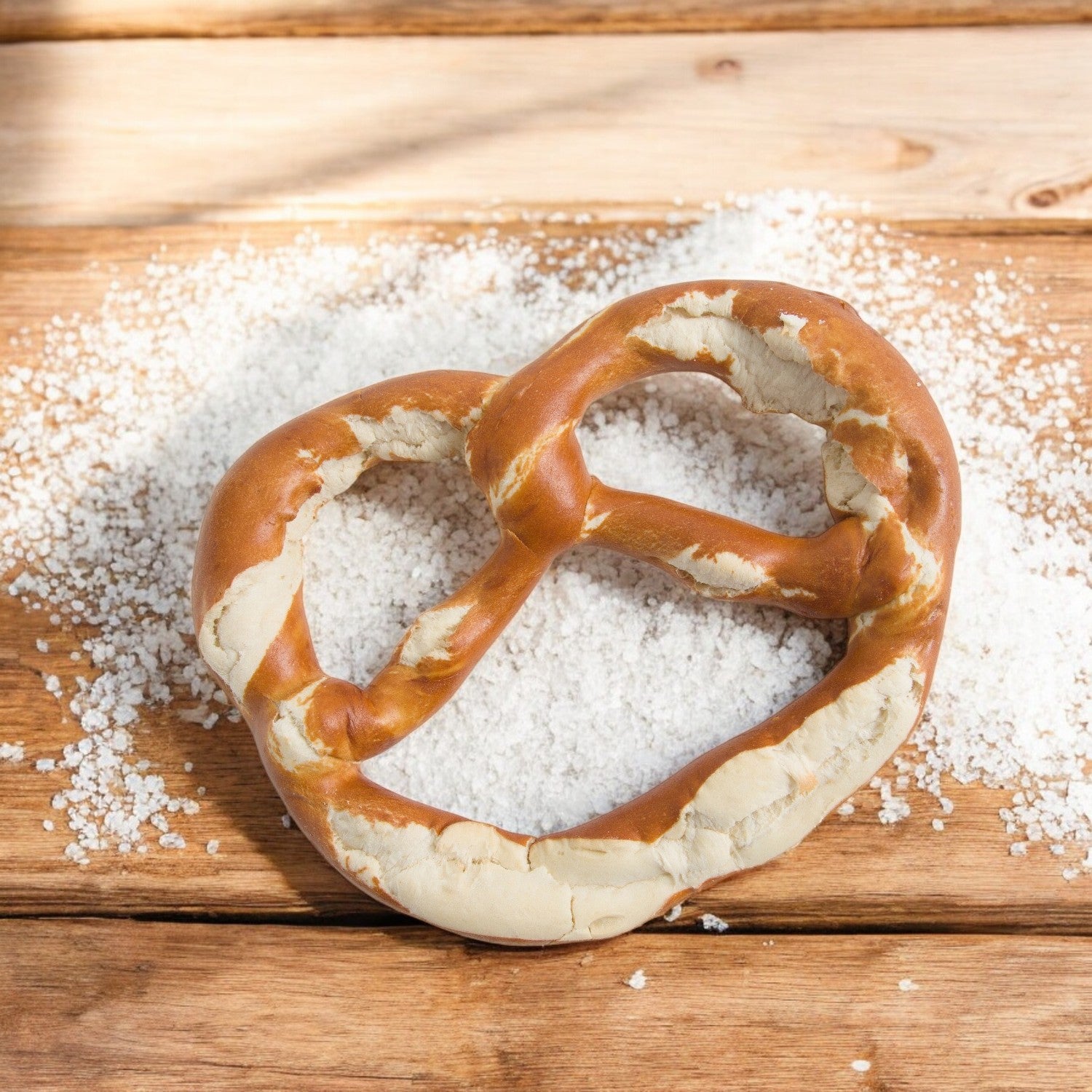 A Prop & Peller Soft Jumbo Pretzel from the 12-pack (10 oz each) rests on a wooden surface, gently salted with coarse salt scattered around.