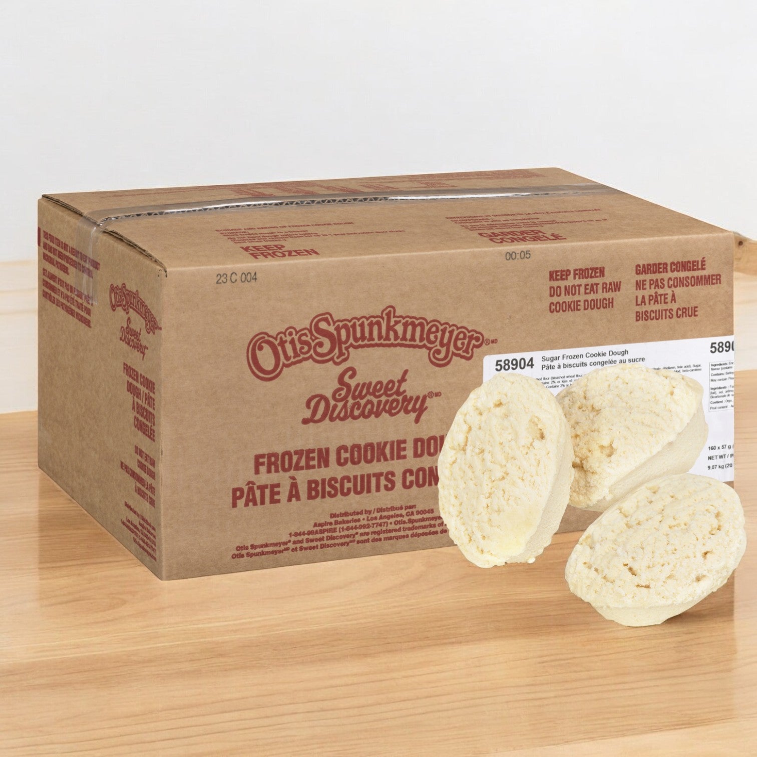 A box of Otis Spunkmeyer Dough Cookie Butter Sugar rests on a wooden surface, suggesting buttery goodness. Two pieces of the enticing dough are placed in front, ready to delight any cookie lover.