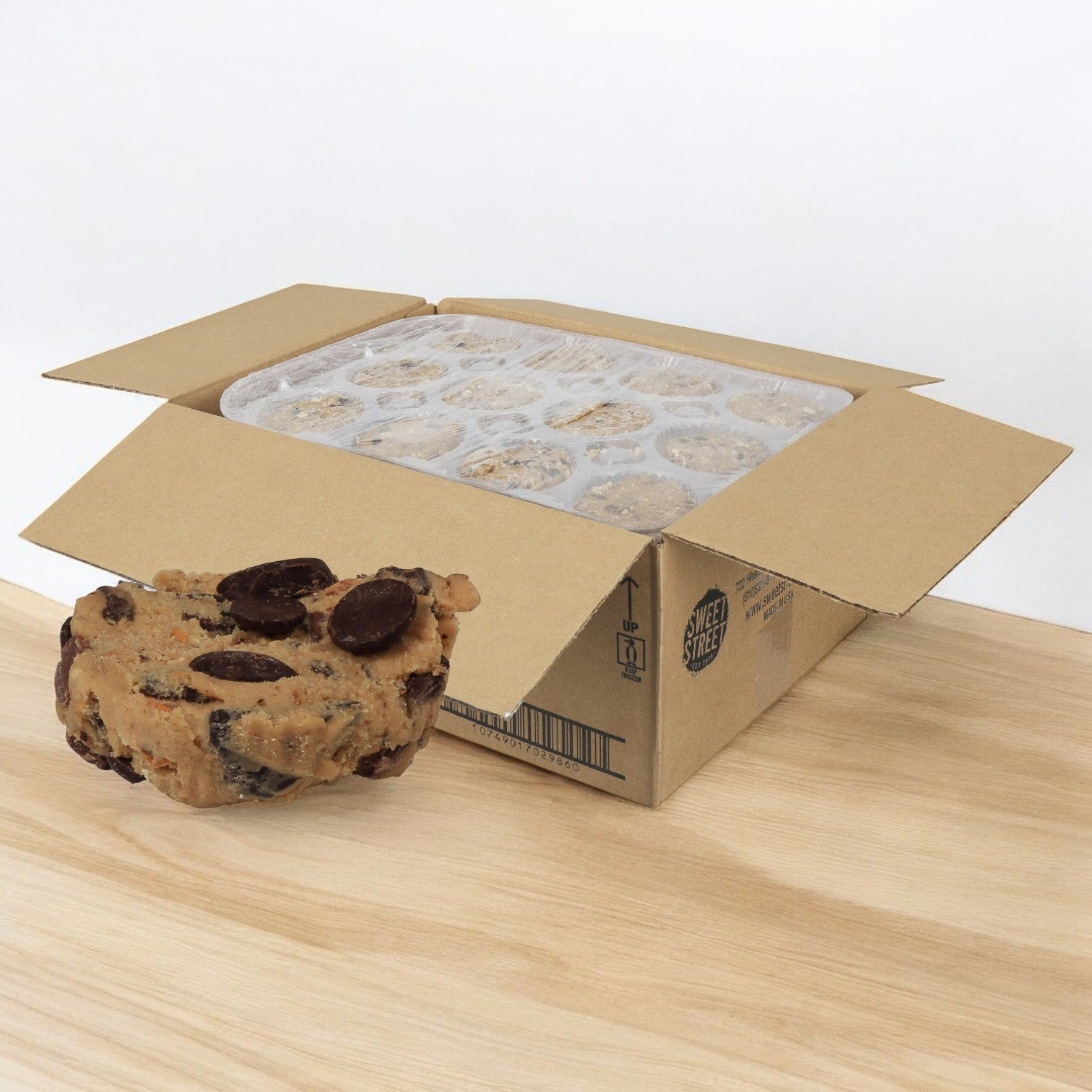 An open box of Sweet Street Dough Cookie Chocolate Chunk from a 48-pack reveals individually wrapped portions, with one unwrapped indulgent treat enticingly resting on the table.