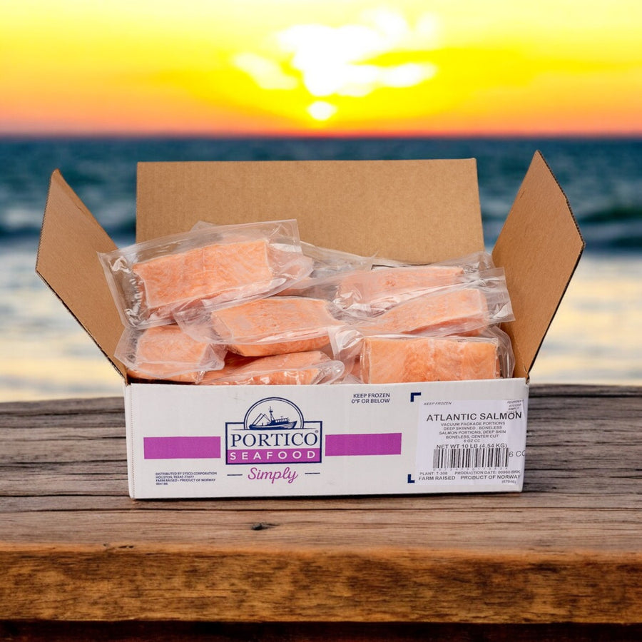 Portico Classic Seafood presents Atlantic Salmon Portions, Skinless, 4 oz - Norwegian in a 10 lbs box, displayed on a wooden surface against an ocean sunset. Packed with Omega-3 fatty acids for a nutritious and tasty meal.