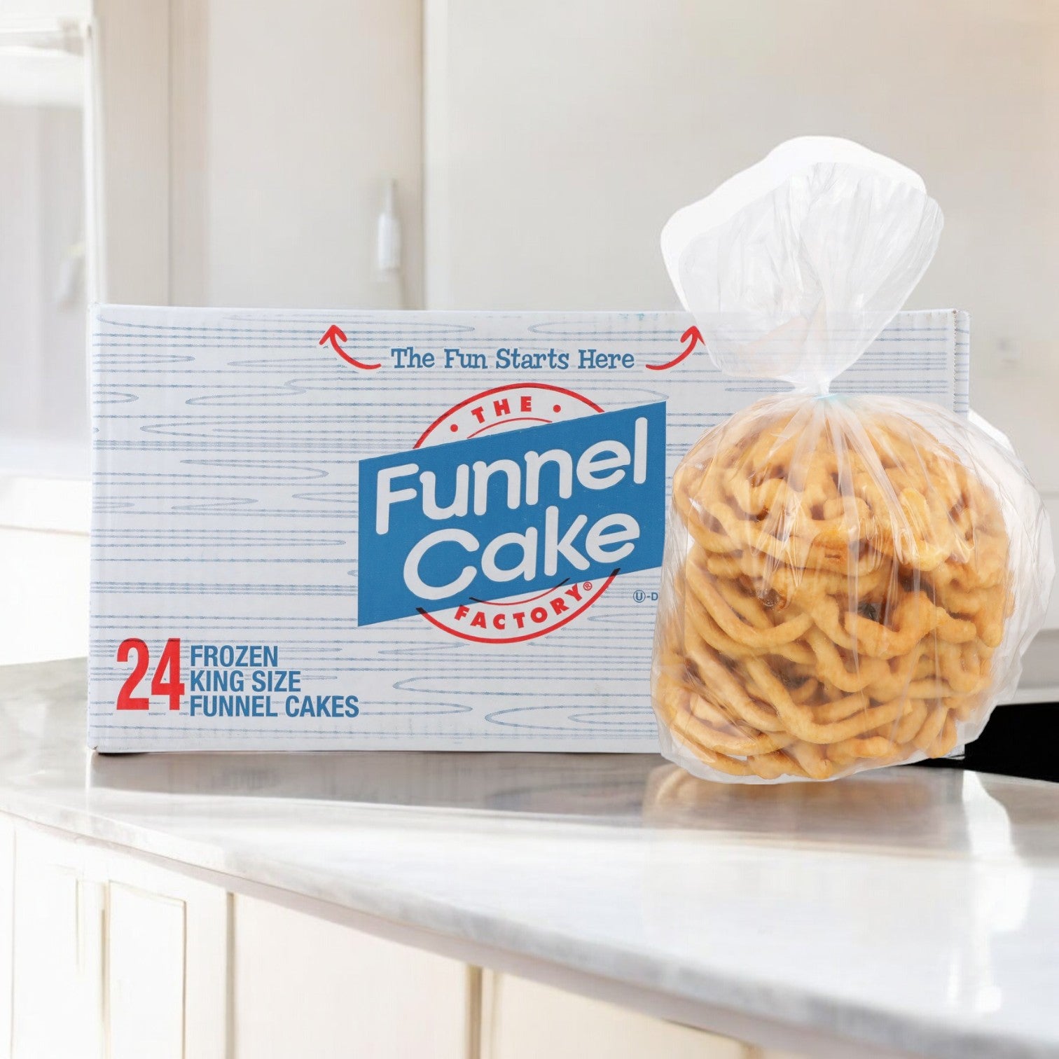 A box of J&j Snacks 8.5" frozen king-size funnel cakes (24 count) sits on the kitchen counter, a sweet treat reminiscent of bustling concession stands, next to a clear bag of tempting funnel cakes.