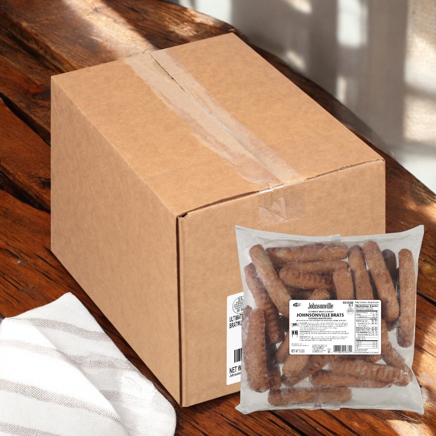 A cardboard box and a sealed plastic package of Johnsonville Foods Bratwurst Pre-cooked Ultimate 5x1 (2/5 LB) are on a wooden table.