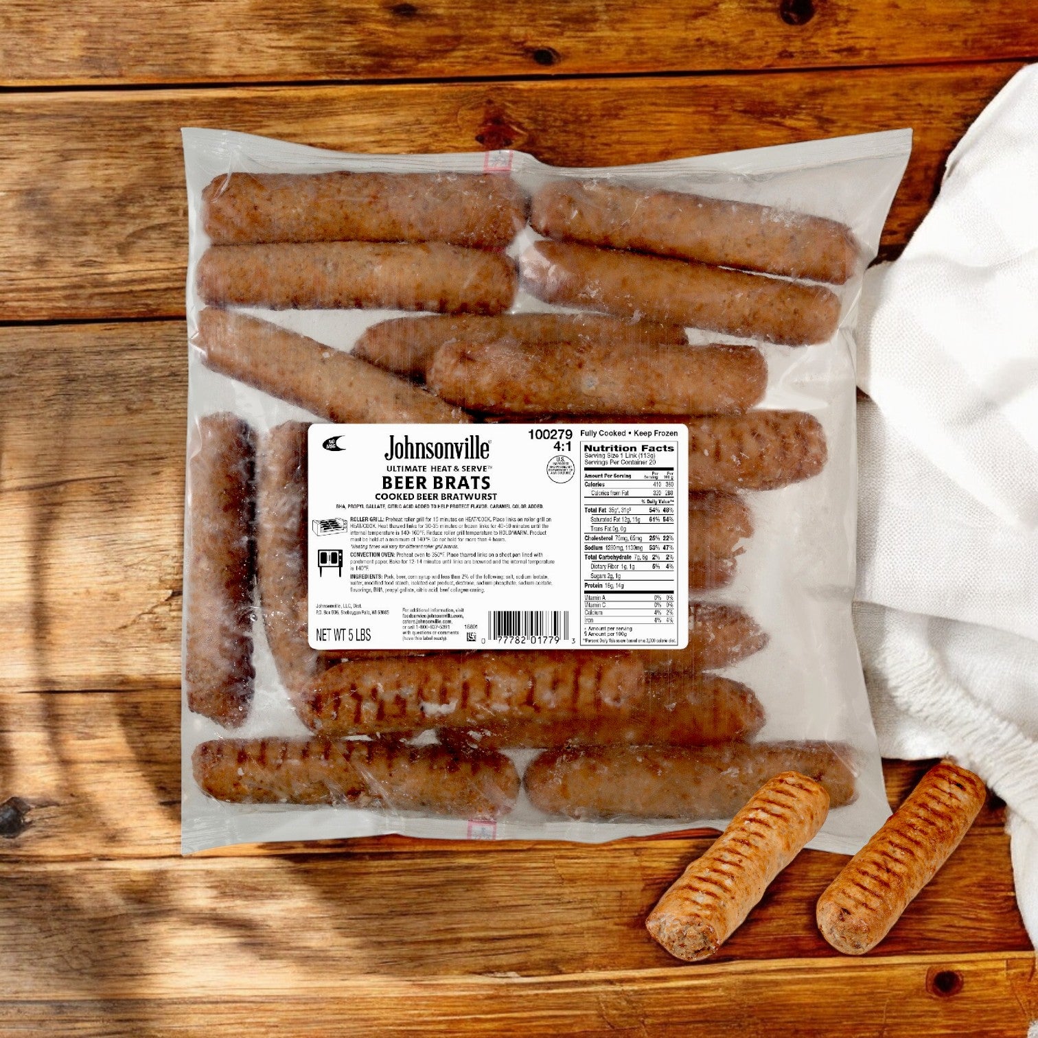 A sealed package of Johnsonville Foods Bratwurst 4 Per # Beer Ultimate (2/5 LB), crafted by the Johnsonville brand, rests on a wooden surface with a white napkin nearby.