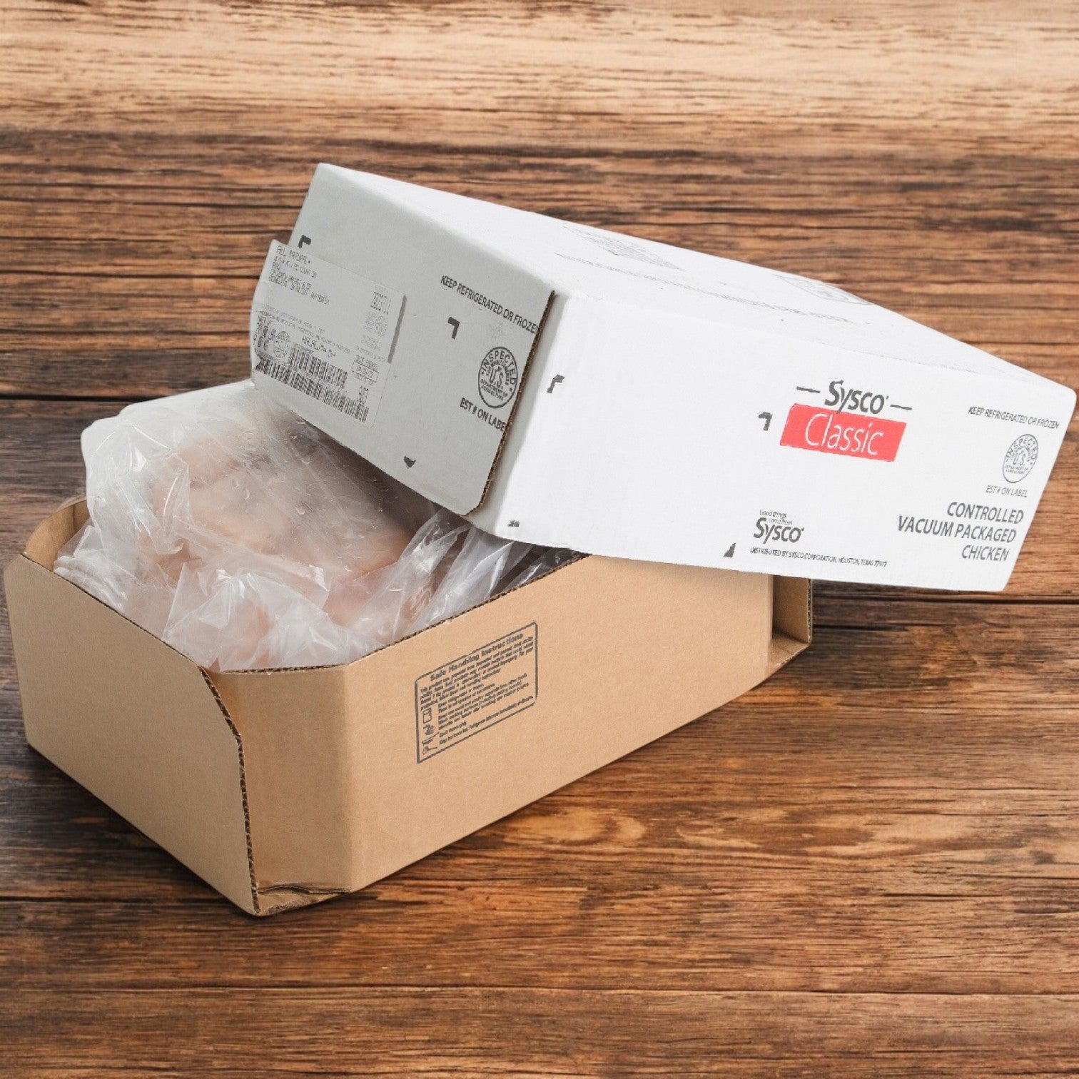 An open cardboard box on a wooden surface reveals vacuum-packaged Sysco Classic Chicken CVP Whole 8 Ounce Halal Breasts. Ideal for foodservice, it provides efficient portion control for culinary needs. Pack Size: 4/5 LB. Brand: Sysco.