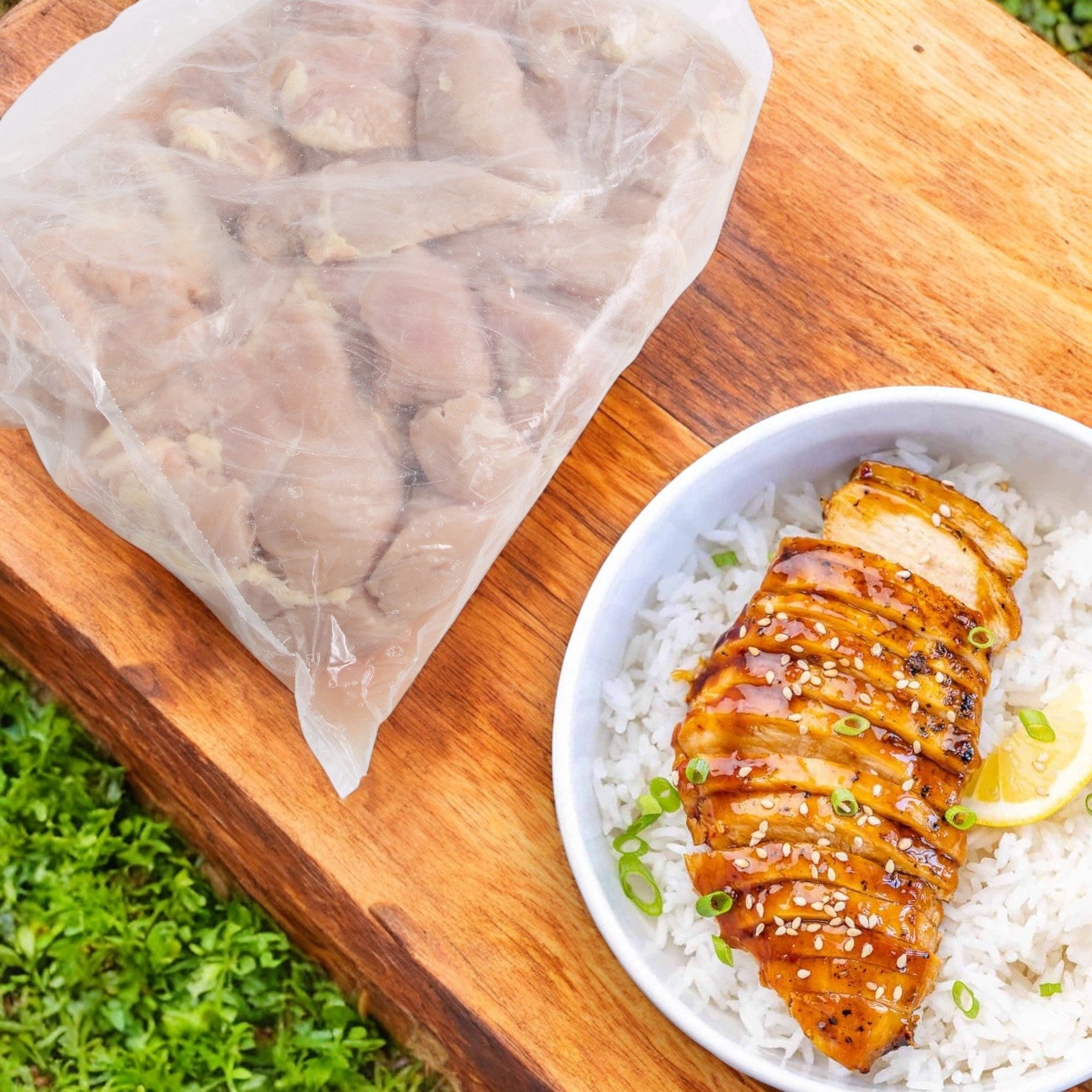 Sanderson Farms, Inc. Chicken CVP Breast Random Halal is grilled with green onions and lemon on rice outside, alongside a bag of raw chicken on a wooden board. Perfect for foodservice, it offers versatility and adapts to random portion sizes. Pack size: 4/10 LB.