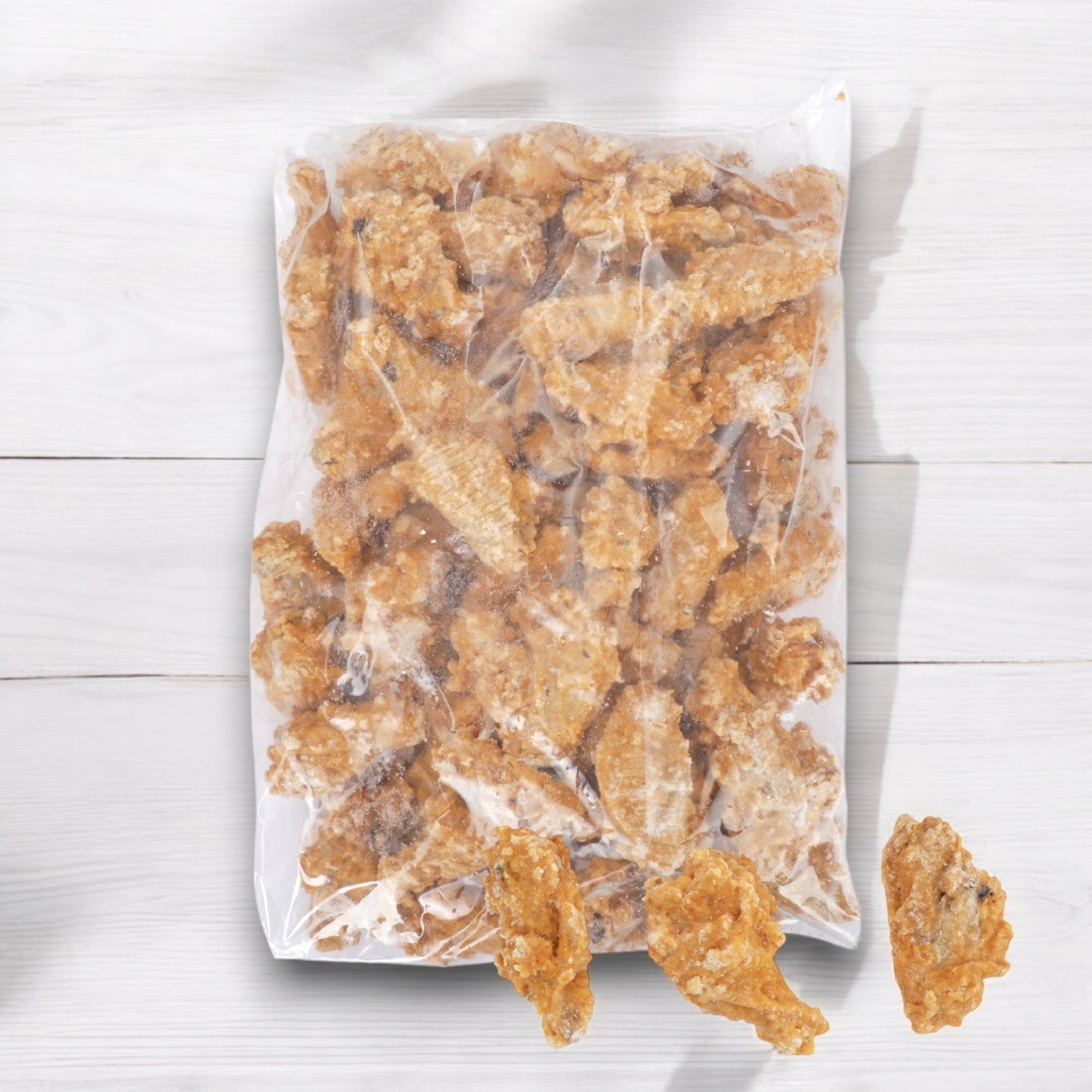 A bag of Pierce (Pilgrim’s Pride) Chicken Wings Breaded Zing Precooked sits on a light wooden surface with three pieces outside the bag. Pack size: 2/7.5 LB.