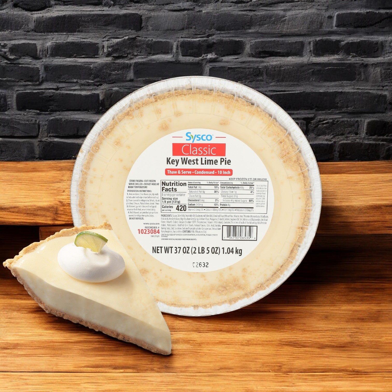 A whole and sliced Sysco Classic Key Lime Pie, Condensed Untopped 6/37 oz., with whipped cream and a lime wedge, evokes tropical flavors against a brick wall backdrop.