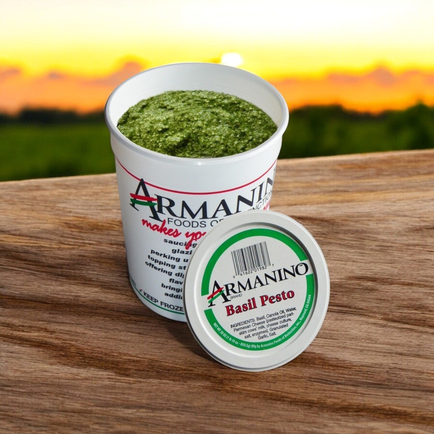 A lid-off container of Armanino Pesto Sauce—Farms Pesto Basil Sauce, 6/30 oz Packs, rests on a wooden surface outdoors with a blurred background. This gluten-free sauce brings authentic Italian flavor to any meal.