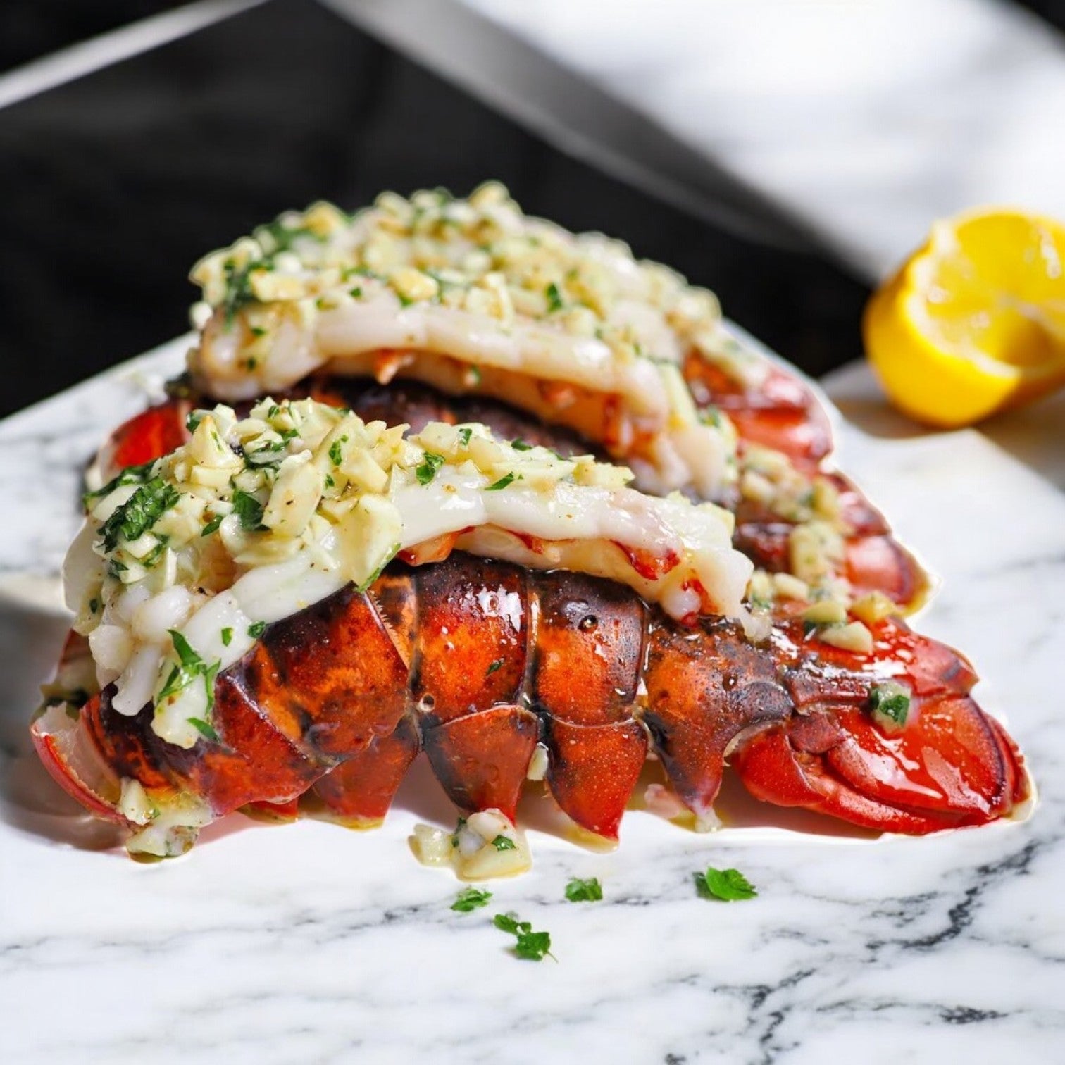 Two 8 oz. Easy Lunches Lobster Tail from Warm Water Nicaragua, topped with herbs and garlic butter, elegantly presented on a white marble plate, accompanied by a lemon wedge.