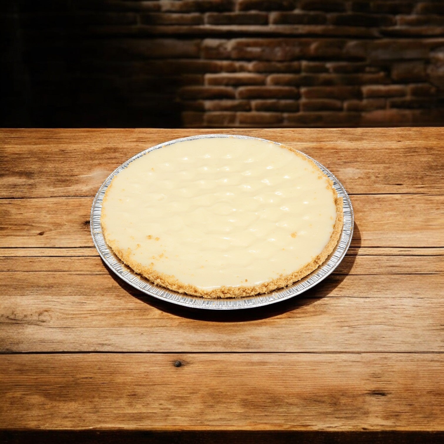 A Sysco Classic Key Lime Pie, with subtle tropical flavors, is elegantly placed on a wooden table against a rustic brick wall backdrop.