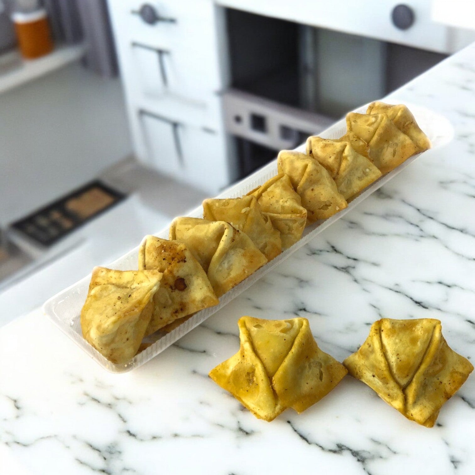 A rectangular plate displays a row of Sysco's classic Crab Rangoon appetizers on a marble countertop, with two extra pastries set aside.