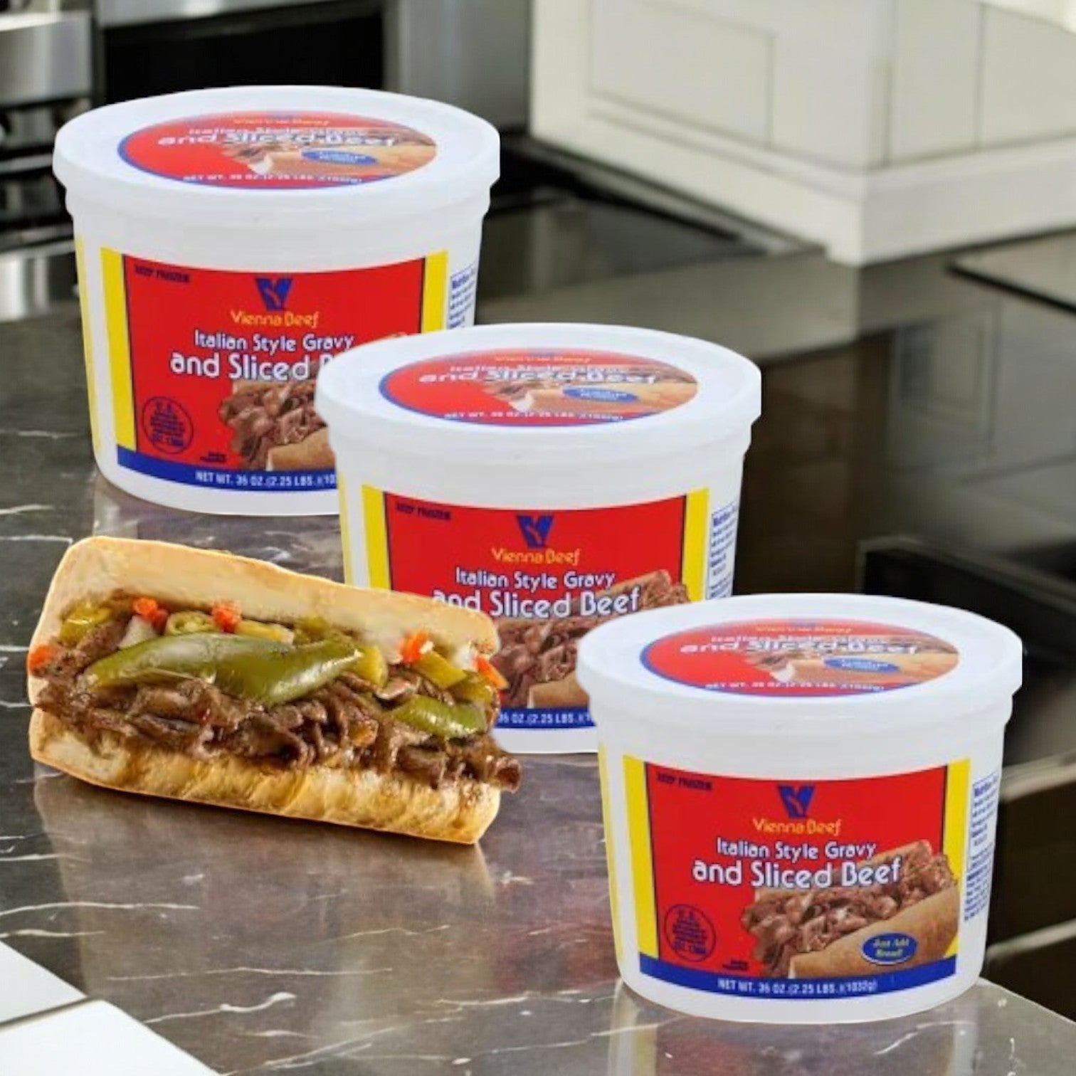 On the counter, there are three containers of "Vienna Beef Italian Style Gravy and Sliced Beef-36oz-3 Count" beside a Chicago-style Italian beef sandwich filled with sliced beef and peppers.