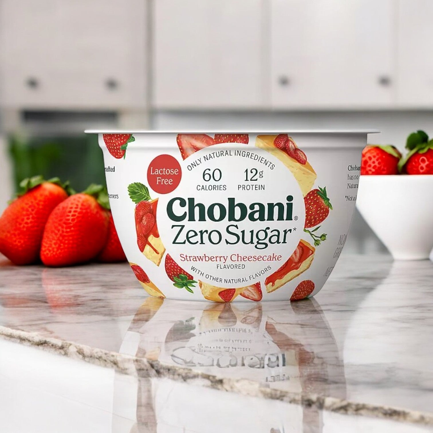 A container from the Chobani Zero Sugar Nonfat Blended Greek Yogurt Variety Pack rests on a marble counter, with fresh strawberries in the background.