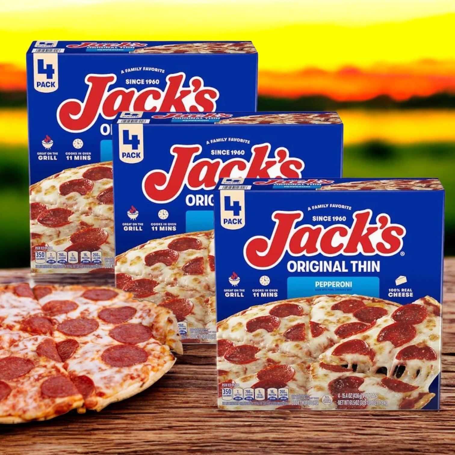 Three boxes of Jack's Original Thin Pepperoni Frozen Pizza, each containing four packs, are on a wooden surface with a freshly cooked pizza topped with savory mozzarella cheese in the foreground.