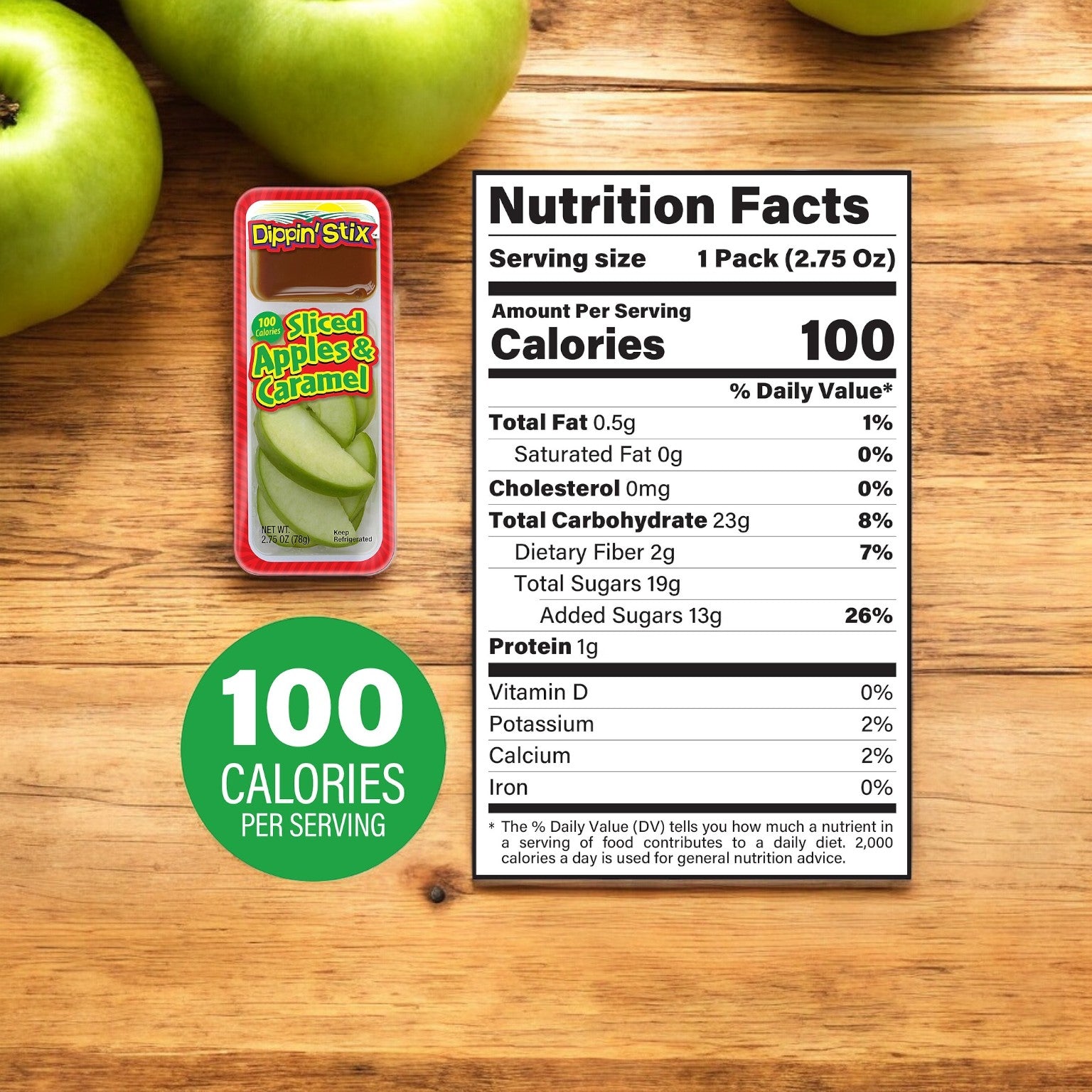 A container of Dippin' Stix Tart Apples & Caramel Snack Packs - 2.75 oz - 1 Count alongside its nutrition facts label on a wooden surface, with green apples in the background. The highlighted text reads "100 CALORIES PER SERVING.