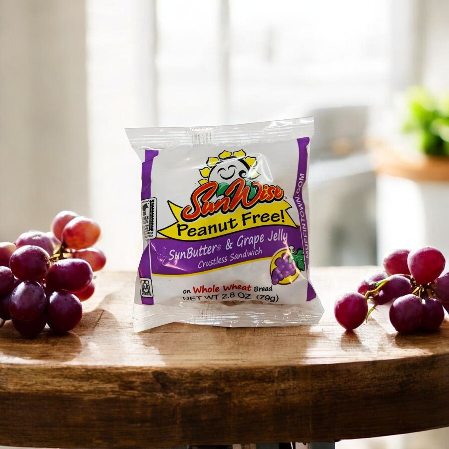 A package of Easy Lunches SunWise Grape Jelly, 2.8 oz - 1 Count crustless PB&J sandwich sits on a wooden surface, accompanied by a bunch of grapes.