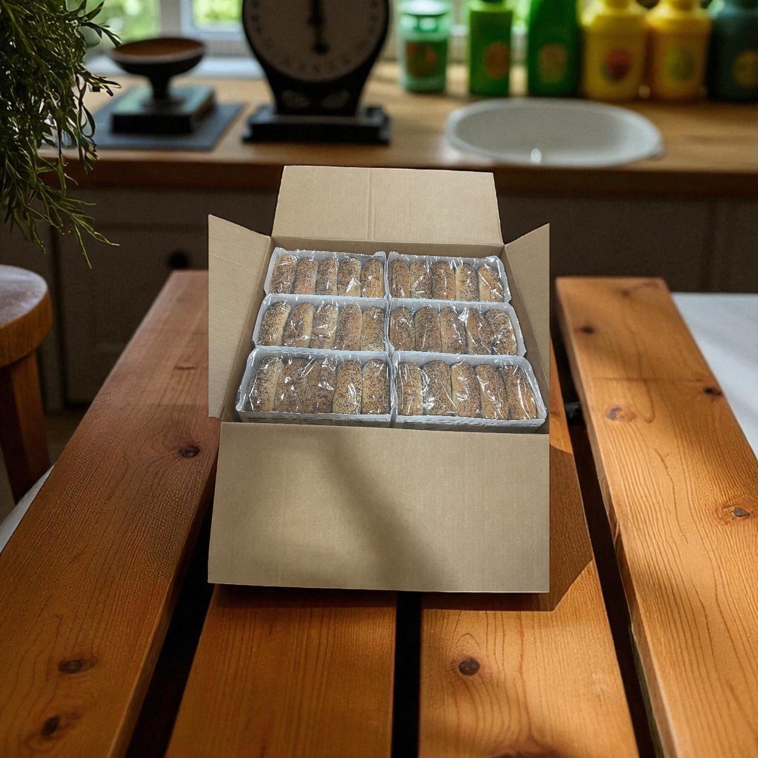 A cardboard box of Vienna Beef Poppy Seed Hot Dog Buns 10 Count - 12 Pack sits open on a wooden kitchen table, with several rows of packaged cookies beside it.