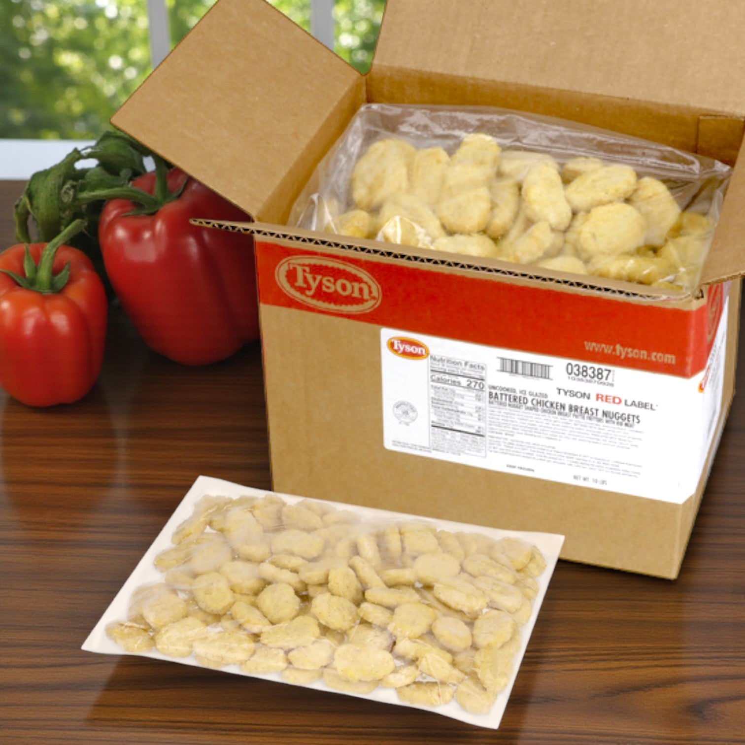 An open box of Tyson Red Label Tempura Battered Chicken Breast Nuggets – 2/5 lb Bags (10 lb Total) from Tyson sits on a table, with a sealed bag of nuggets and two red bell peppers nearby.