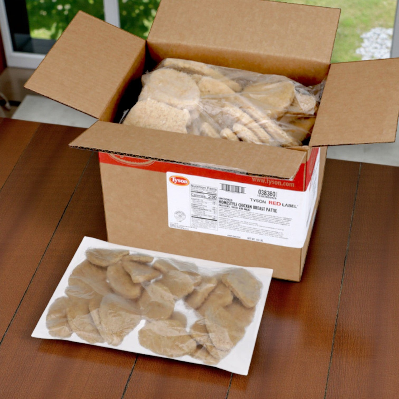 A box of Tyson Red Label Breaded Homestyle Chicken Breast Patties – 2/5 lb Bags (10 lb Total) sits on a wooden table, with the chicken patties visible in plastic-wrapped trays.