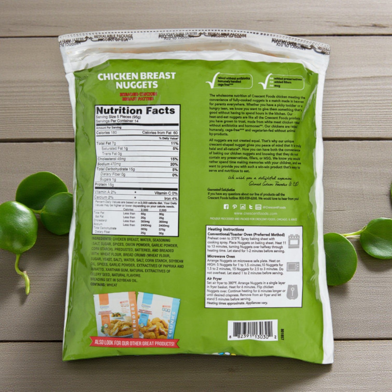 Back of a green Crescent Foods Halal Chicken Breast Nuggets – 3 lbs bag on a wooden surface, displaying nutrition facts, ingredients, product description, heating instructions, and images of other Crescent Foods products.