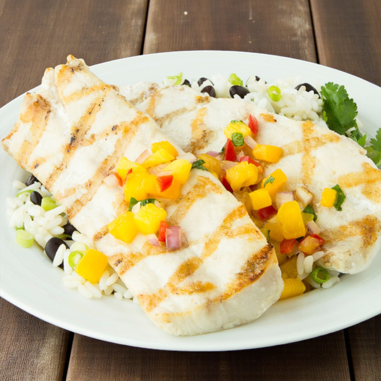 Orca Bay Seafood Mahi Mahi Medallions (1–3 oz) are served grilled with mango salsa atop rice and black beans, garnished with green onions—a delicious premium seafood dish from Orca Bay Seafood.